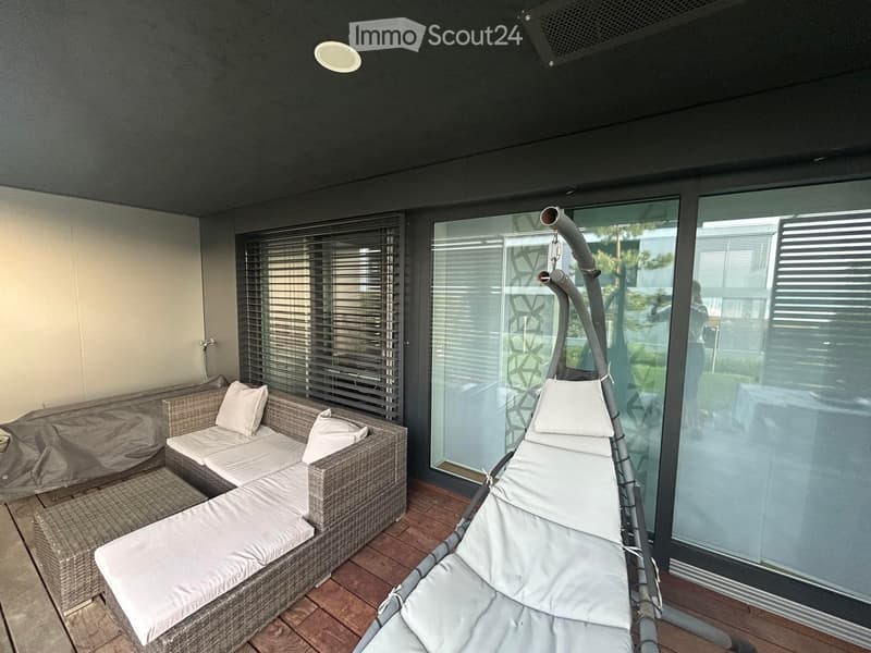 Outdoor patio with a sofa, swing, and a table. The sofa has cushions and a cover.