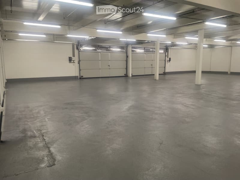 Unfurnished Room. Empty room with concrete floor, white walls, and overhead lighting. Two large garage doors are visible.