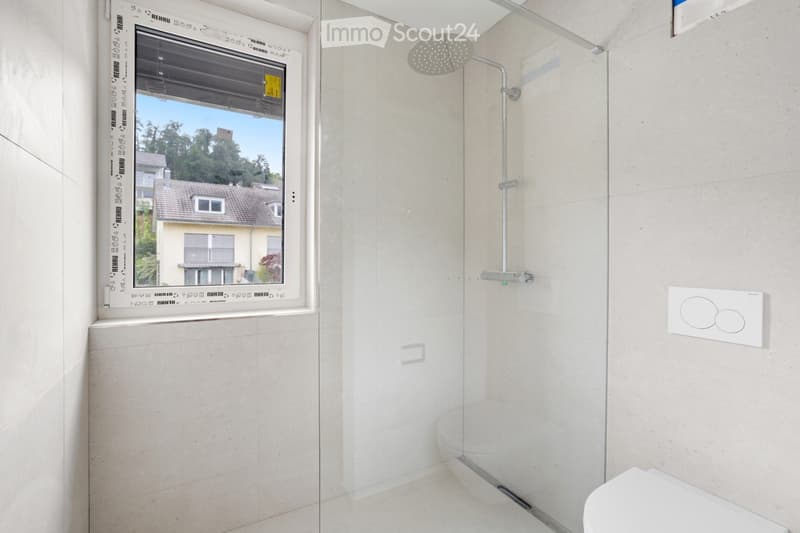 Modern bathroom with a large window offering a view of the outside, featuring a toilet, a showerhead with a handheld sprayer, and a control panel for water temperature and flow.