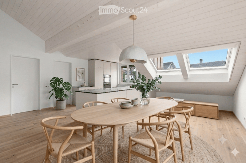 Bright, open dining area with a large wooden dining table surrounded by six chairs, a pendant light fixture, a kitchen counter with a potted plant, and a vase with greenery on the table.