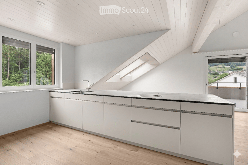 Modern kitchen with white cabinets, a central island, and large windows offering a scenic view of greenery and a distant landscape.
