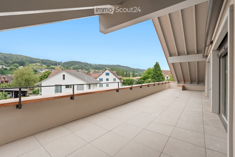 Balcony with tiled floor, wooden railing, and scenic view of a town and hills in the background.