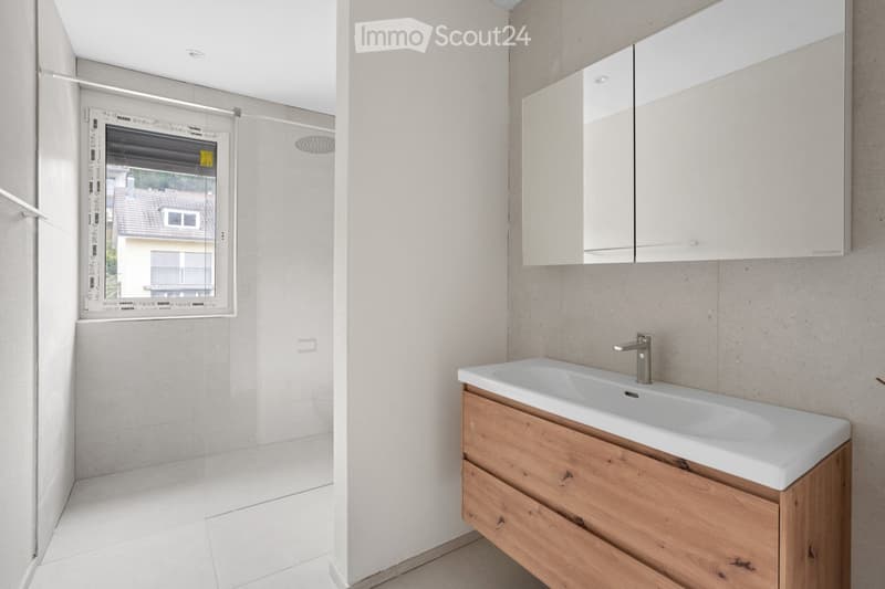Modern bathroom with a white sink, wooden cabinet, mirror, and a shower area with a glass door.