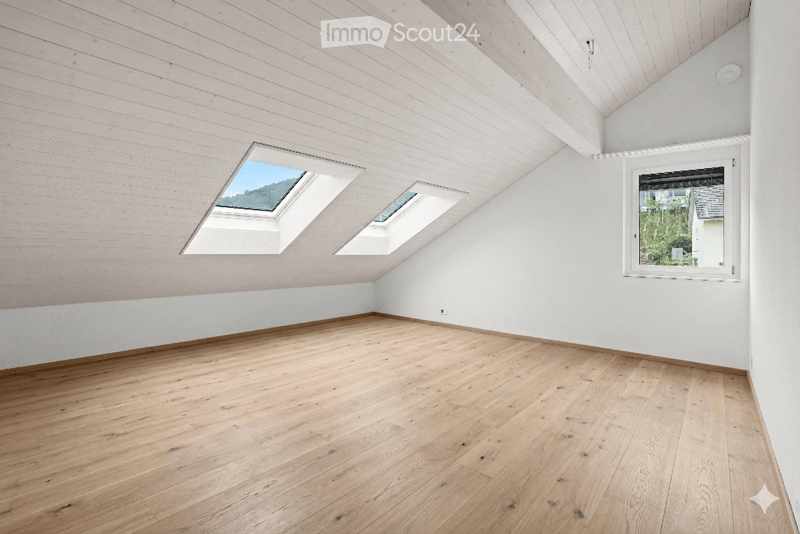 Bright, empty attic room with wooden flooring, white paneled walls and ceiling, and skylights providing natural light.