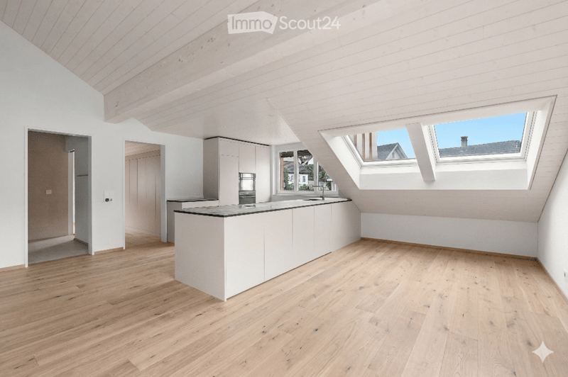 Bright, open kitchen with white cabinetry, a central island, wooden flooring, and skylight windows offering natural light and a view of the roof.