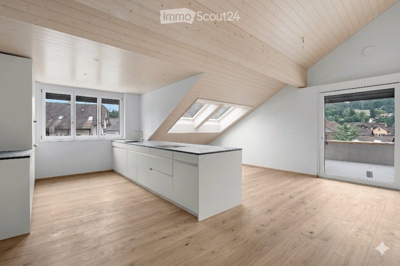 Bright, open kitchen with white cabinetry, a central island, wooden flooring, large windows, and a skylight. The space is empty, with no furniture or appliances.