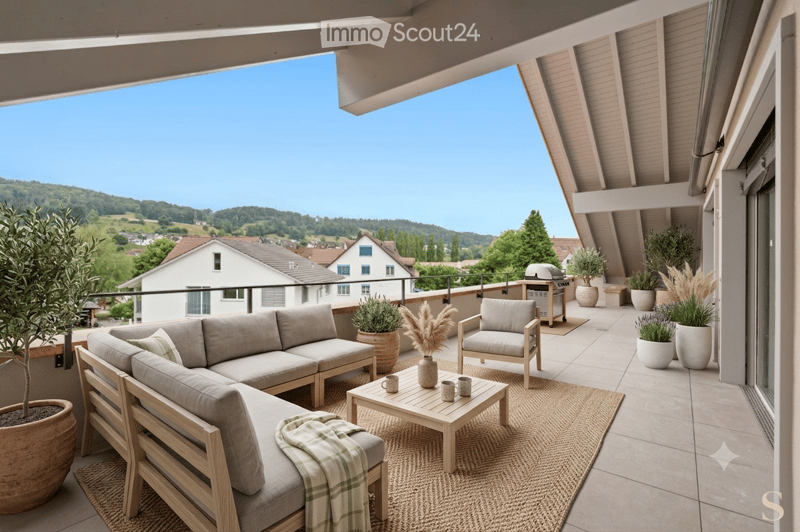Balcony with a view of a countryside landscape, featuring a grey sofa, wooden coffee table, armchairs, and potted plants.