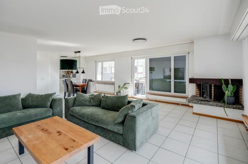 Spacious living room with white tiles, green couches, wooden coffee table, and a fireplace with a cactus plant.