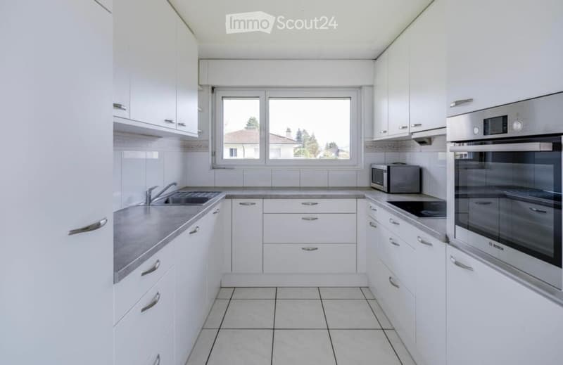 Modern kitchen with white cabinets, granite countertops, stainless steel appliances, and a large window.