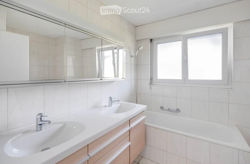 Bathroom with white tiles, double sinks, mirror, bathtub, and shower head.