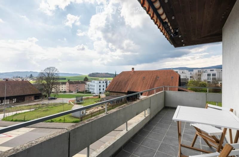 Outdoor balcony with a table and chairs, overlooking a scenic view of the town and countryside.
