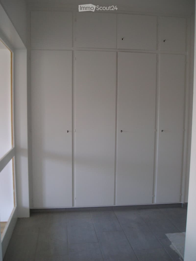An empty room with white walls and tiled floor, featuring a row of white built-in cabinets.