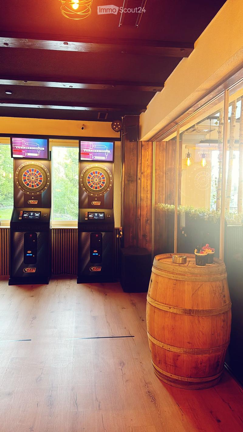 A stylish room with wooden floors, dartboards, screens, and a barrel table with a flower pot.