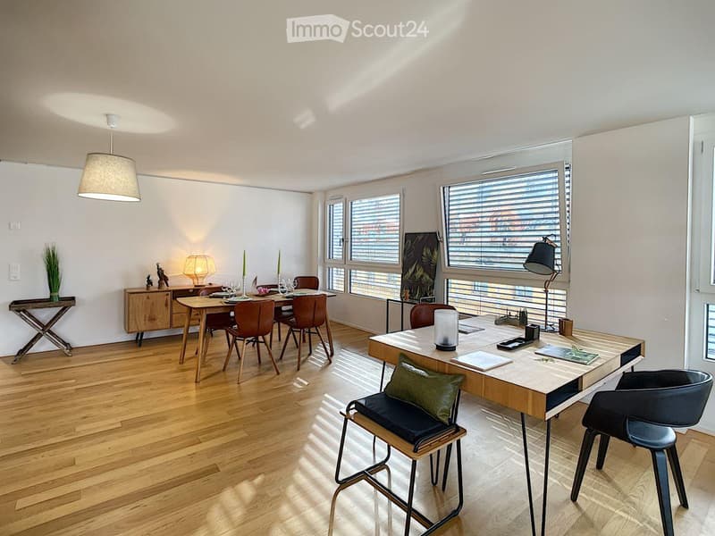 Spacious room with wooden floors, a dining table set for a meal, a desk with a lamp, and various decorative items.