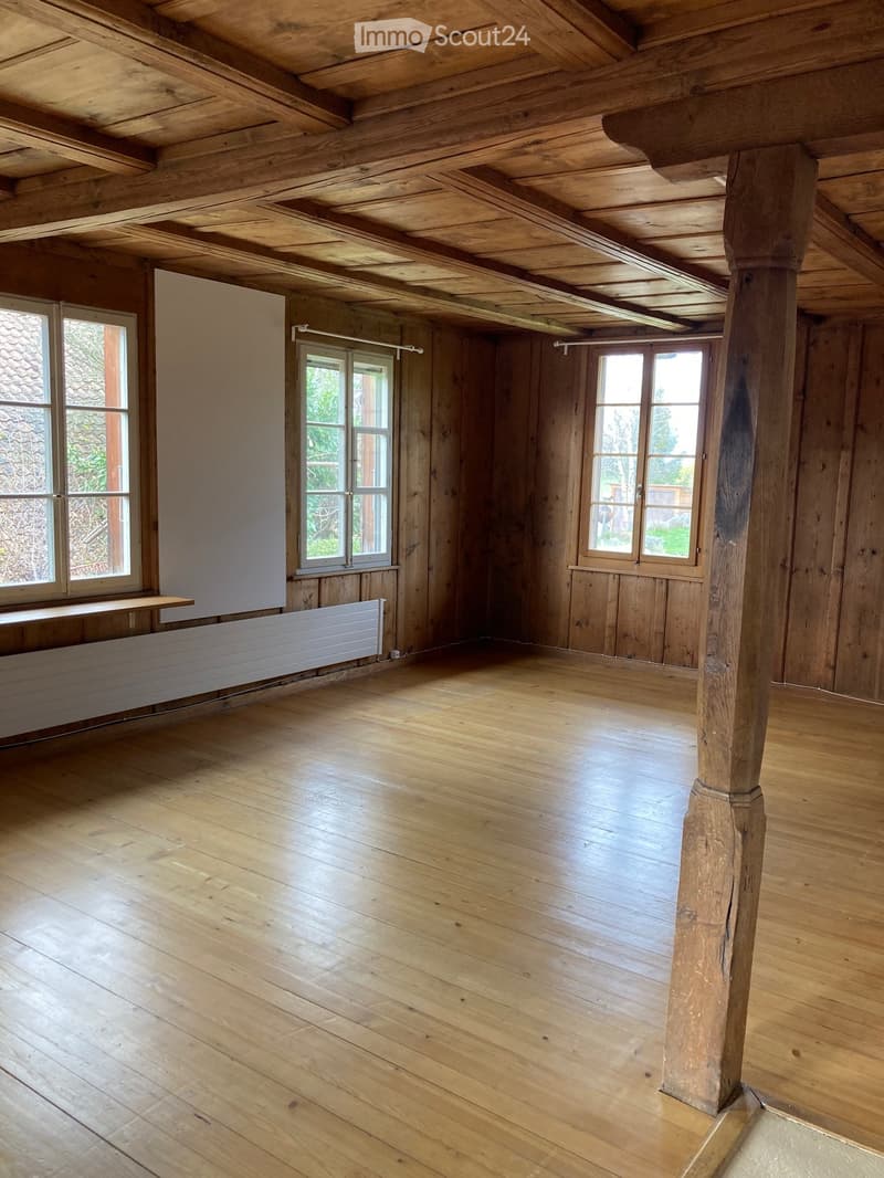Unfurnished Room. Empty room with wooden walls, wooden floor, and three windows. A wooden beam and a wooden pillar are visible.