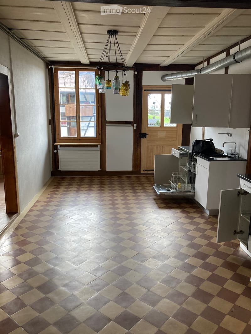 Kitchen. Empty kitchen with checkered tile floor, wooden door, white cabinets, and a sink with a faucet. A dishwasher is open, and a lamp hangs from the ceiling.