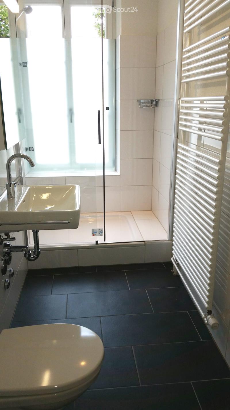 Modern bathroom with white tiles, black floor, glass shower enclosure, white sink, and toilet.