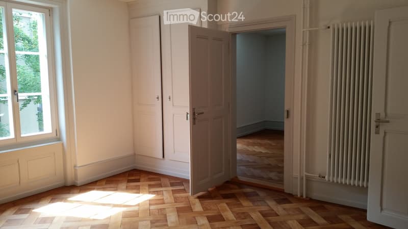 Empty room with wooden parquet flooring, white walls, and doors. Sunlight coming through the window.