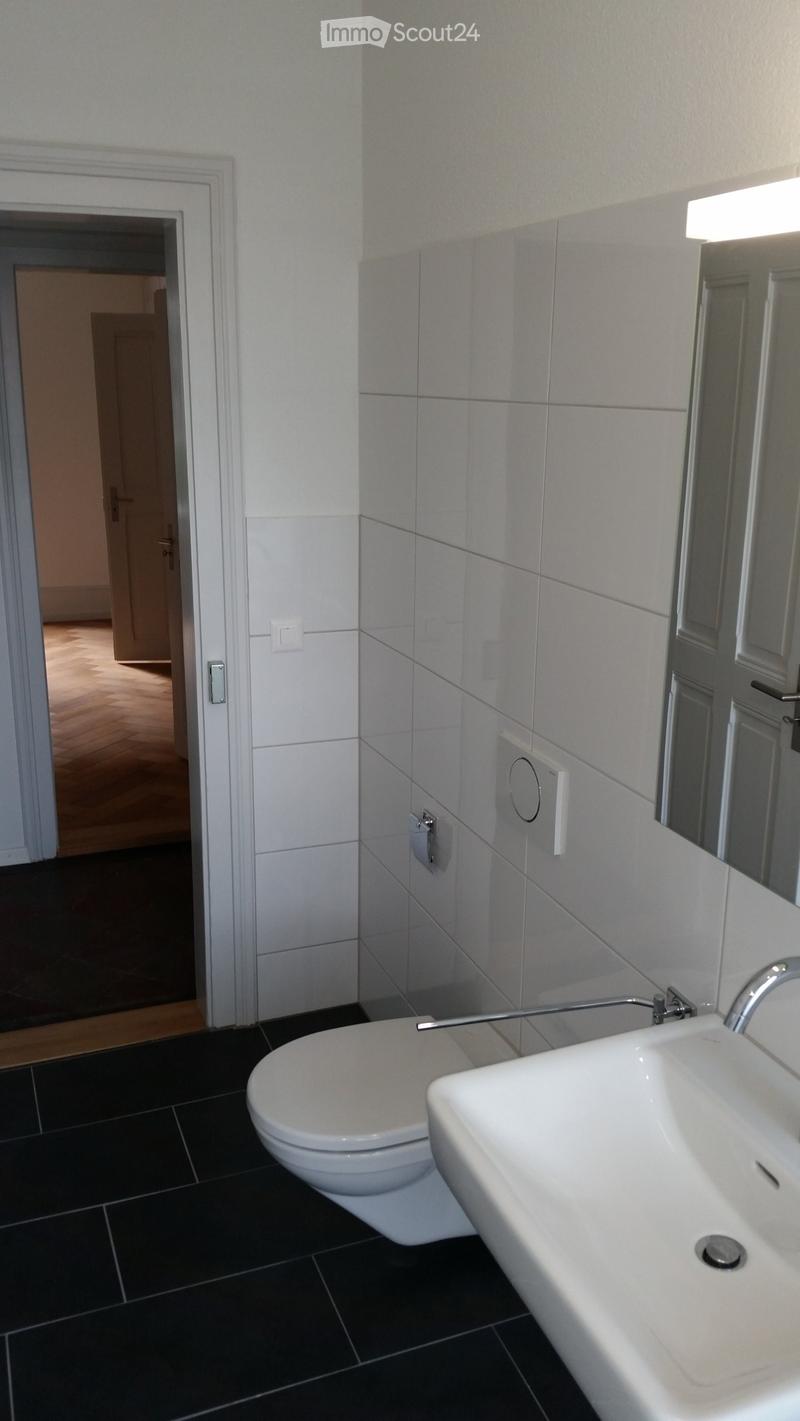 Bathroom with white tiles, black floor, white toilet, sink, mirror, and faucet.