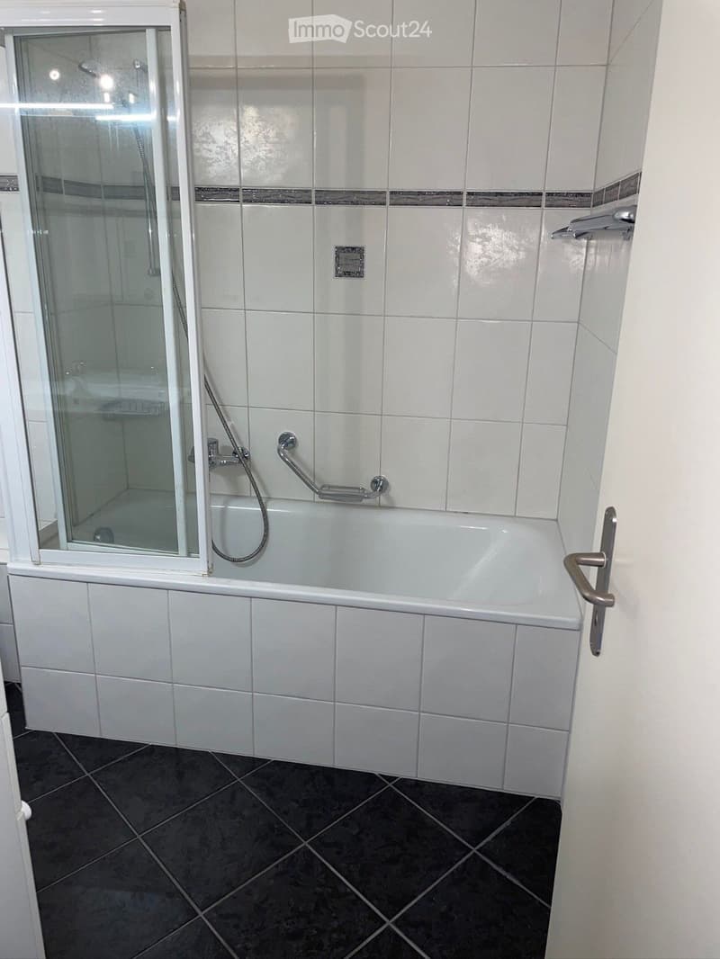 Bathroom with white tiles, bathtub, shower, and black tiled floor.