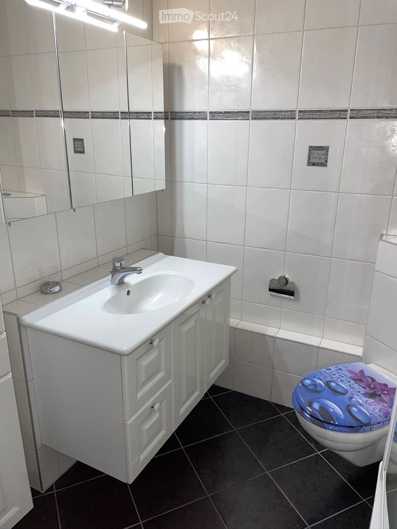 Bathroom with white tiles, white sink, white toilet, white cabinet, mirror, and glass cup