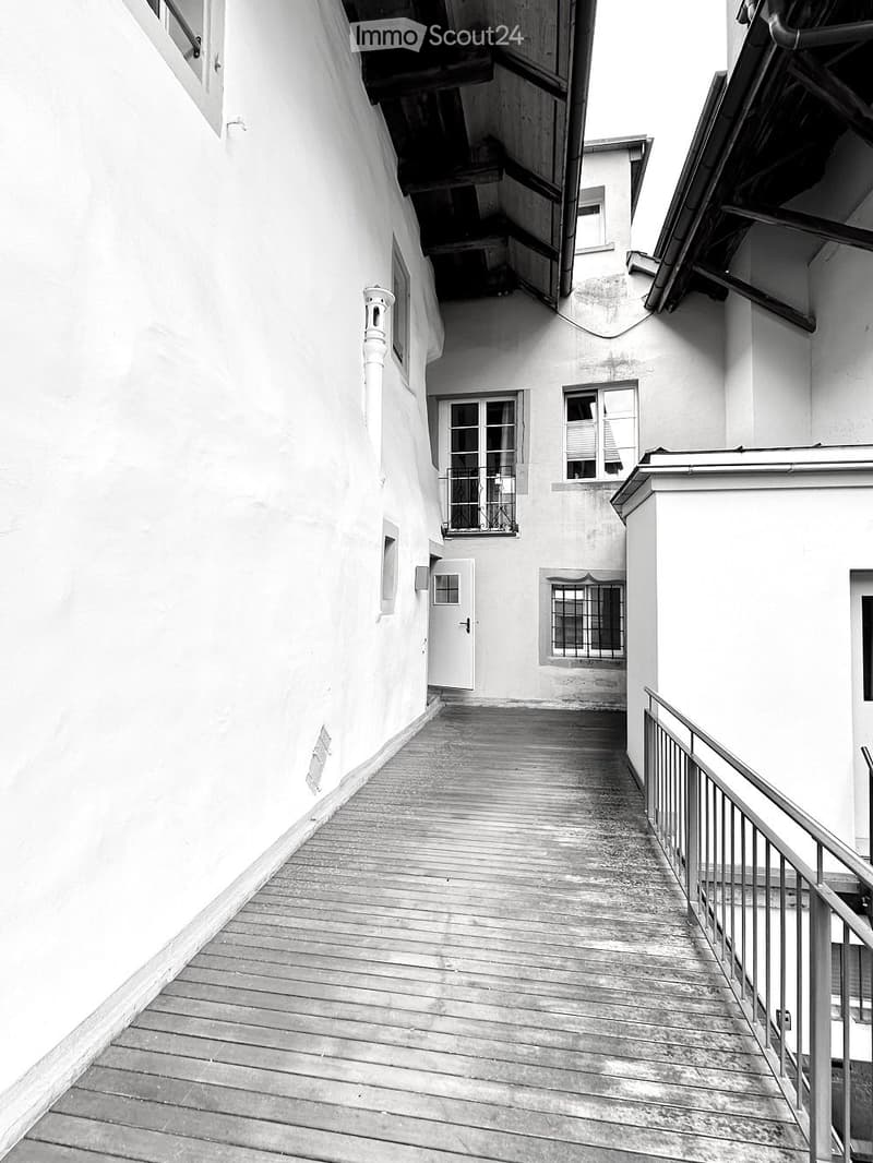 Exterior of a building with wooden walkway, white walls, balconies, and windows