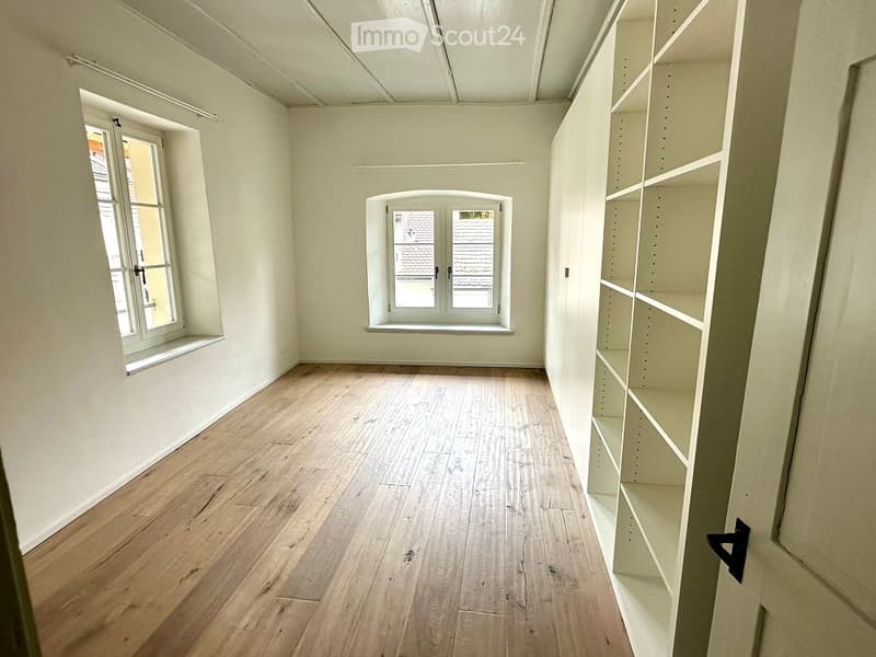 Empty room with hardwood floors, two windows, white walls, and white shelves.