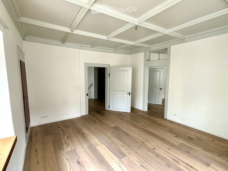 Empty room with hardwood floor, white walls, white doors, white ceiling with beams, power outlet on the wall