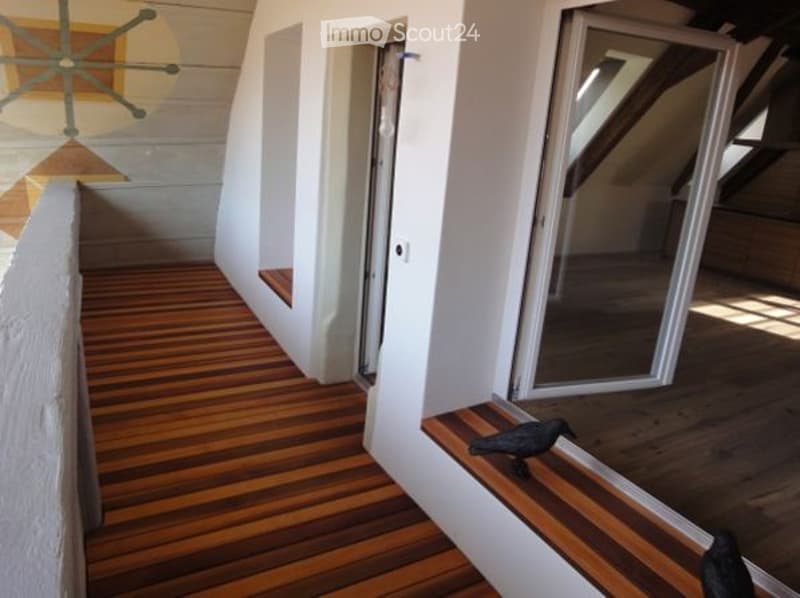 Balcony with wooden flooring, large windows, small bench, white walls