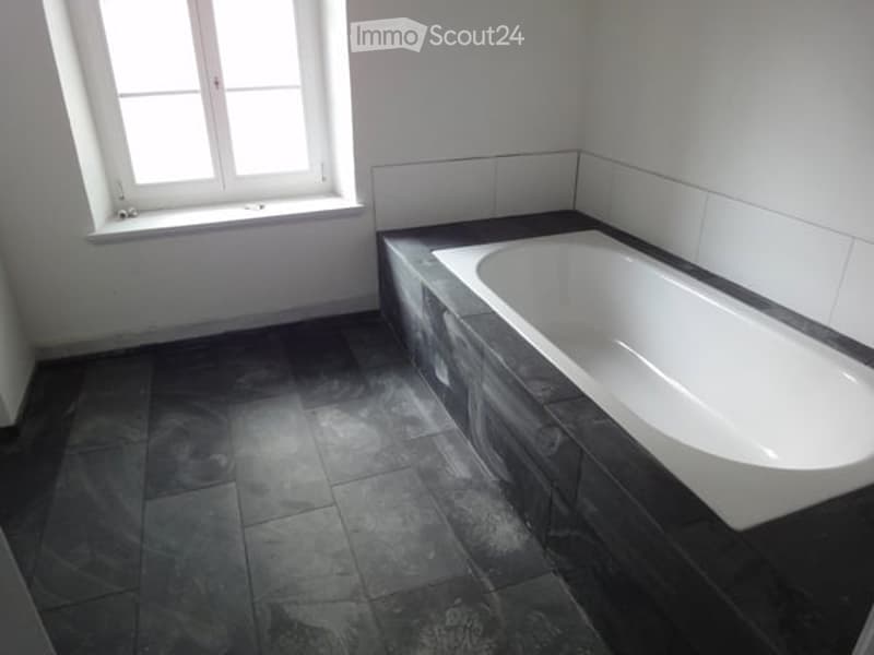 White bathtub, tiled floor, white walls, window with wooden frame