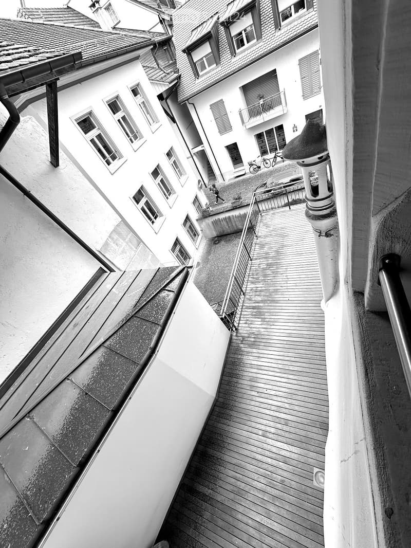 Exterior view of a building with multiple stories, each with many windows. The building has a tiled roof and balconies on some windows. The buildings have railings and stairs.