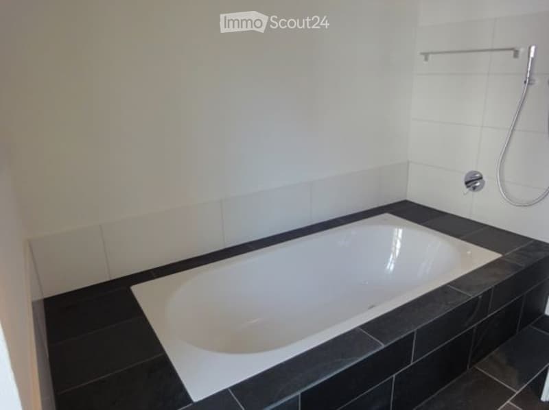 bathroom with a white bathtub, black tiles, white walls, and a shower with a stainless steel hose