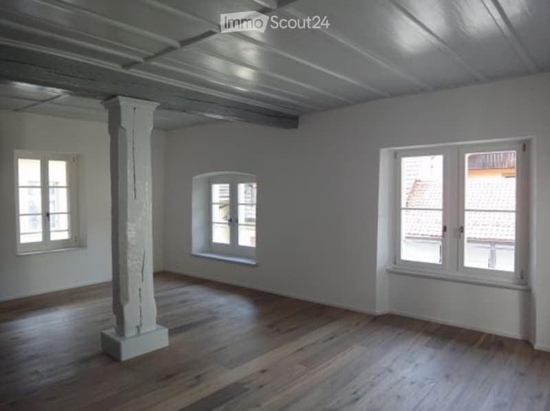 Open floor with white walls, wooden floor, white beams and large windows