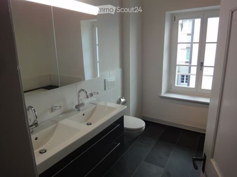 Bathroom with double sink, toilet, window, large mirror and white tiles