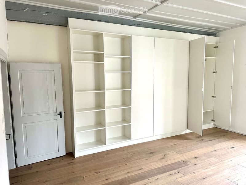 empty room with white wall, wooden floor, large white built-in cabinets
