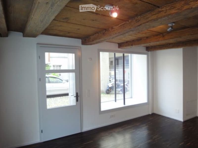 room with wooden beams, wooden floor, white walls, double doors, large windows