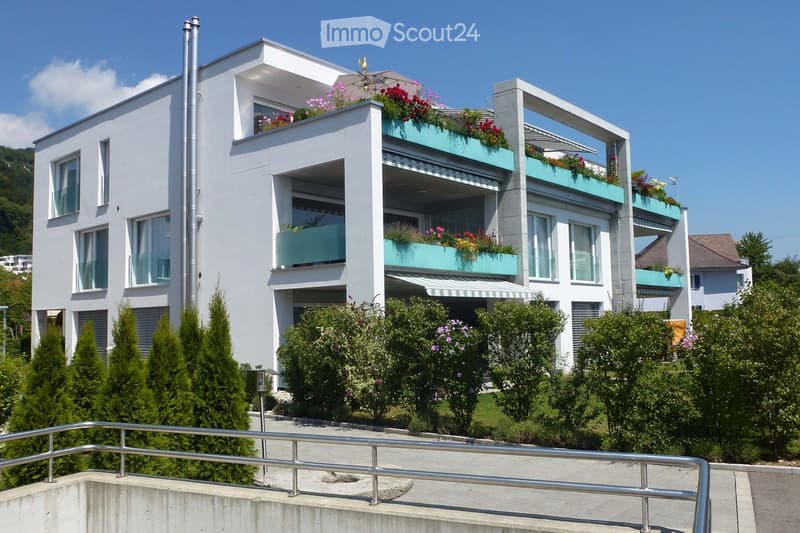 white building, 3 stories, 5 balconies, plants, trees, bushes