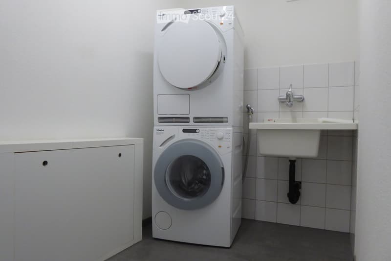 laundry appliances in a room with white wall, floor and tiles, a cabinet and a sink