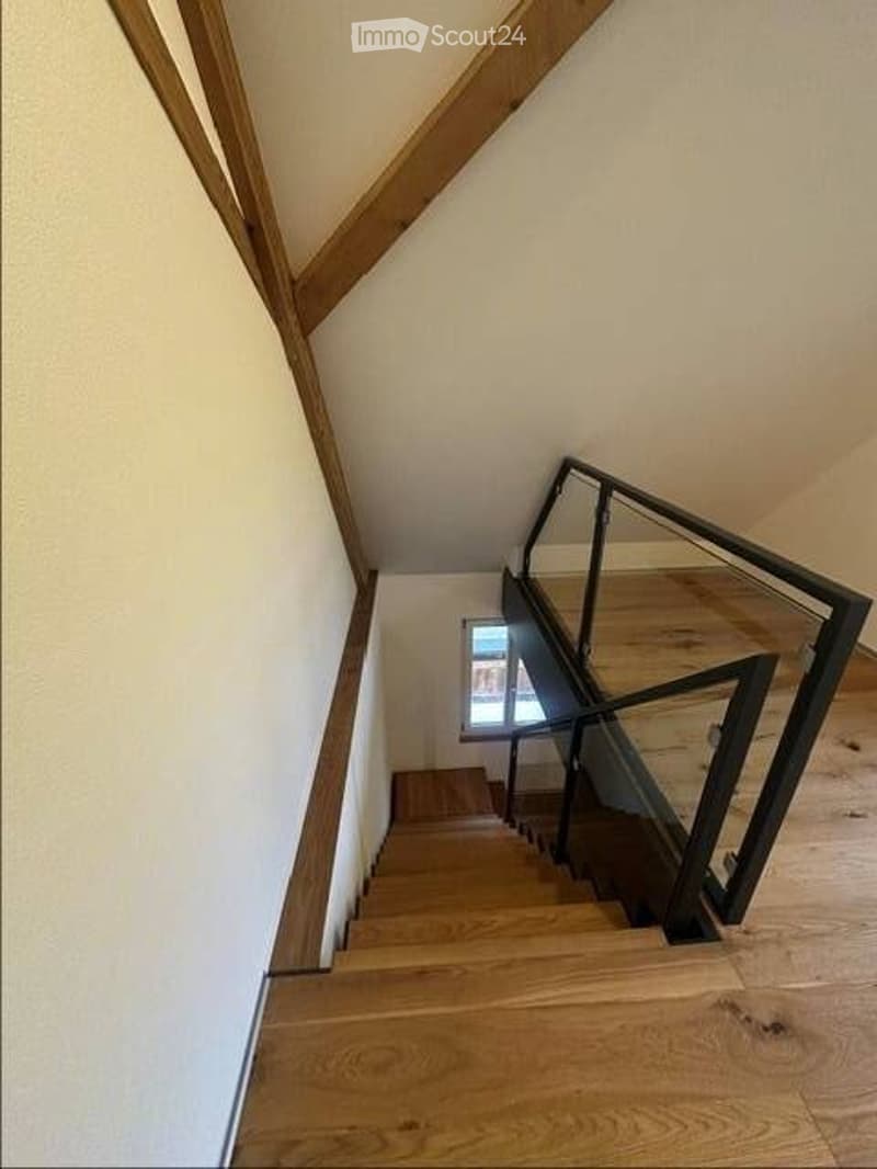 A modern staircase with wooden steps and a glass railing, leading to an upper floor.