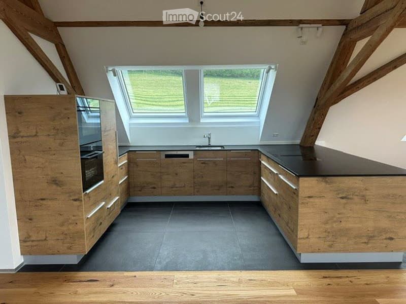 Modern kitchen with wooden cabinets, black countertops, and a sink with a faucet. The kitchen includes an oven and a microwave. The floor is wooden, and the ceiling features wooden beams.
