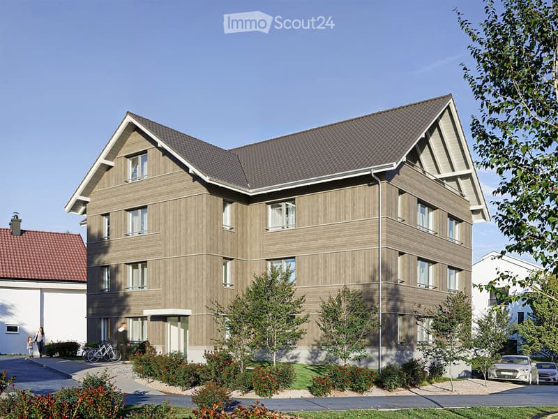 3 story apartment building, gray walls, brown roof, several windows, driveway with parked cars