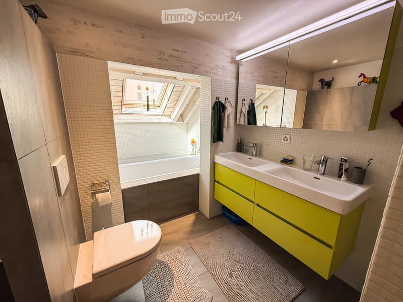 Bathroom with bathtub, double sink, yellow cabinets, white tiles, skylight, and a toilet.