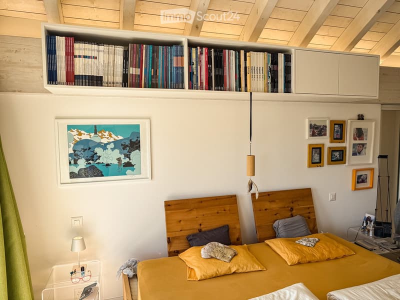 bedroom with two beds, wooden headboards, yellow bedding, wooden ceiling, shelves with books, picture frame, lamps, nightstands, green curtain