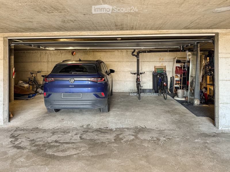 underground parking space with a blue car, bicycles, and storage items