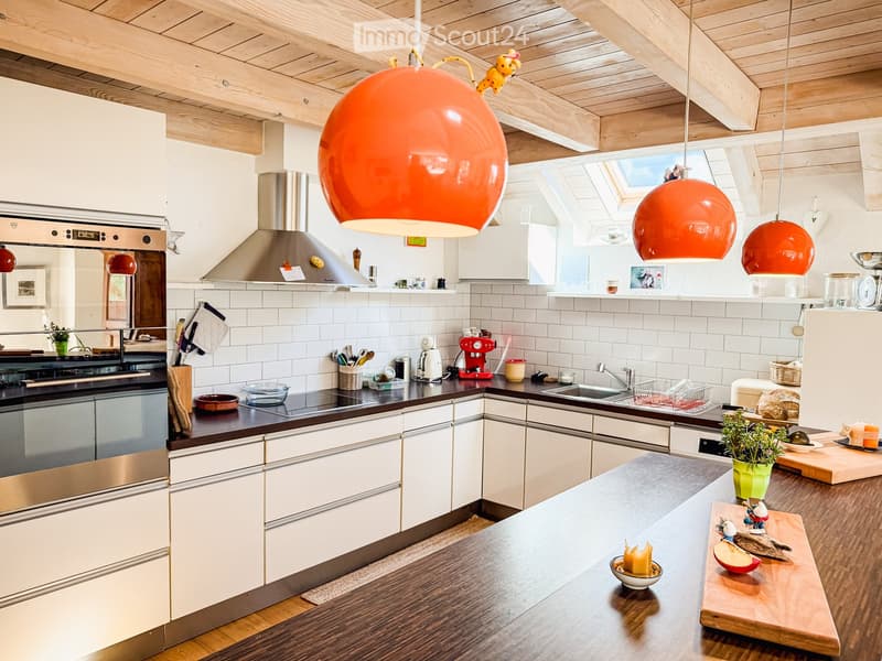 modern kitchen with white cabinets, black countertops, orange pendant lights, stainless steel appliances, white tiled backsplash, wooden ceiling beams, skylight