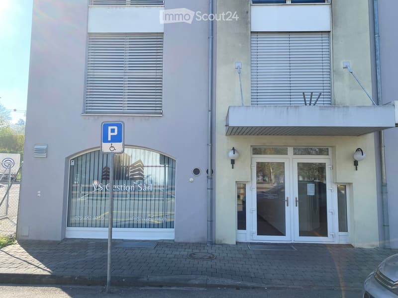 Building. Facade of a building with two entrances, one with a glass door and the other with a glass window. A parking sign is in front of the building.