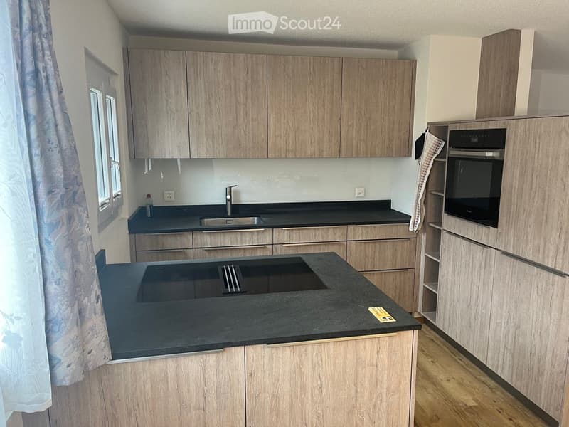 Kitchen. Modern kitchen with light wood cabinets, black countertops, stainless steel sink, and built-in oven.