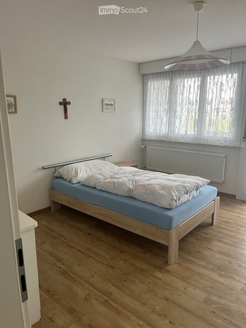 Bedroom. Bedroom with wooden flooring, a single bed with blue mattress and white bedding, a nightstand, a radiator, a cross on the wall, and a picture frame.
