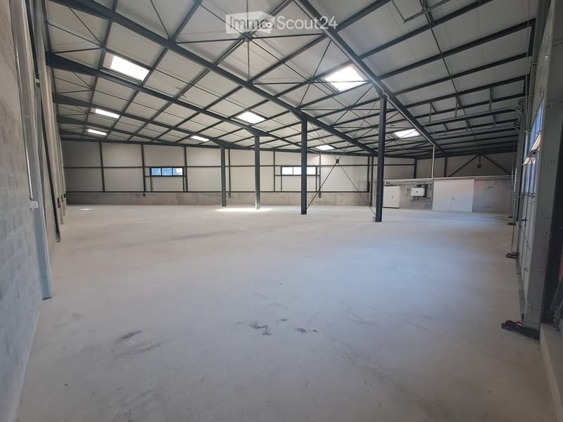 Large, empty industrial-style space with a high, metal-framed ceiling and concrete floor. Minimal lighting and no furniture or equipment.