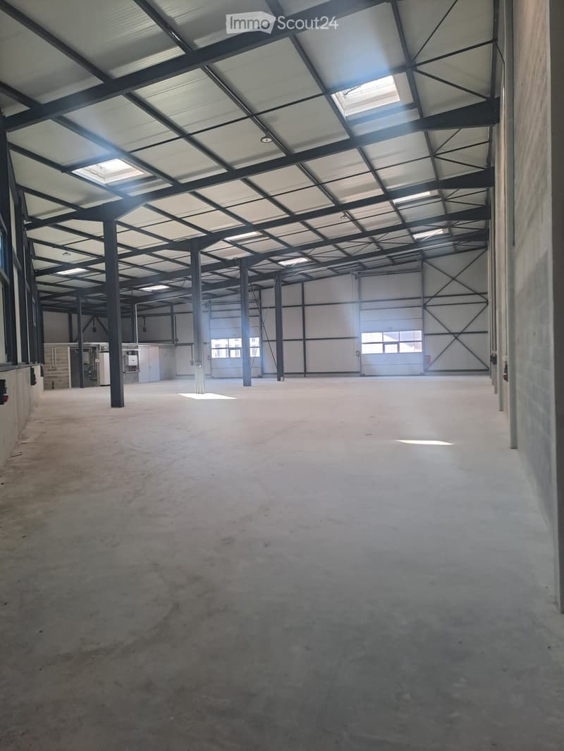 Large, empty industrial-style space with a high ceiling, metal beams, and concrete floor. Minimal lighting and no furniture.